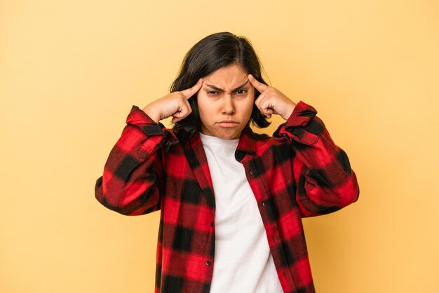 Jeune femme latine isolée sur fond jaune concentrée sur une tâche, gardant les index pointant la tête.