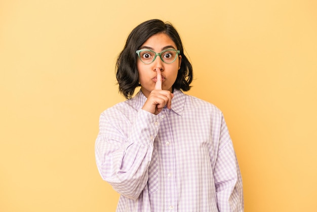 Jeune femme latine isolée sur fond jaune gardant un secret ou demandant le silence.