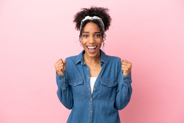 Jeune femme latine isolée sur fond rose célébrant une victoire en position de vainqueur