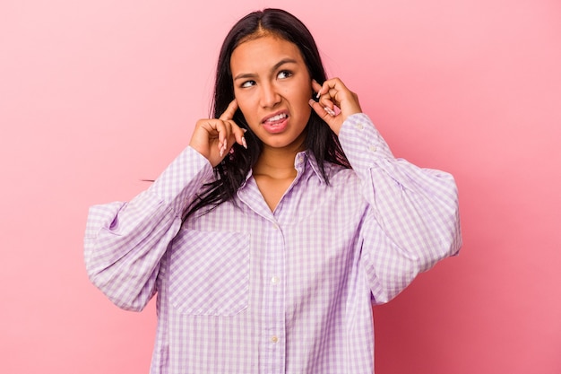 Jeune femme latine isolée sur fond rose couvrant les oreilles avec les doigts, stressée et désespérée par une ambiance bruyante.