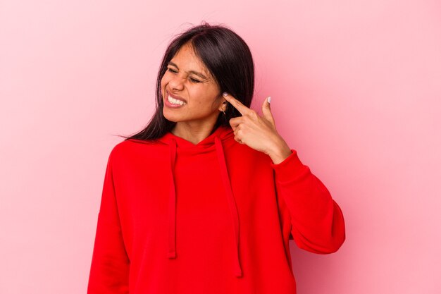 Jeune femme latine isolée sur fond rose couvrant les oreilles avec les mains.