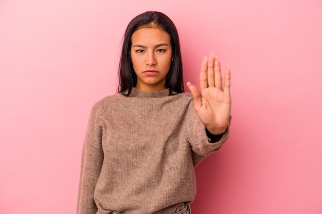 Jeune femme latine isolée sur fond rose debout avec la main tendue montrant le panneau d'arrêt vous empêchant