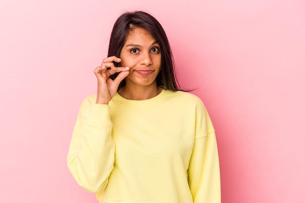 Jeune femme latine isolée sur fond rose avec les doigts sur les lèvres gardant un secret.