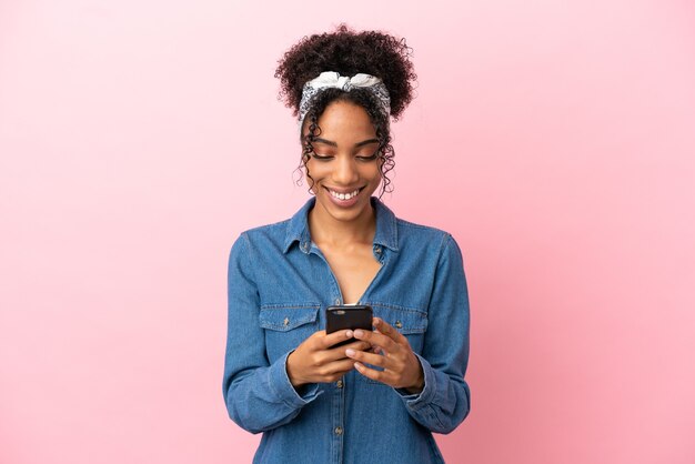 Jeune femme latine isolée sur fond rose envoyant un message avec le mobile