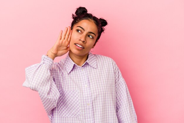 Jeune femme latine isolée sur fond rose essayant d'écouter un potin.