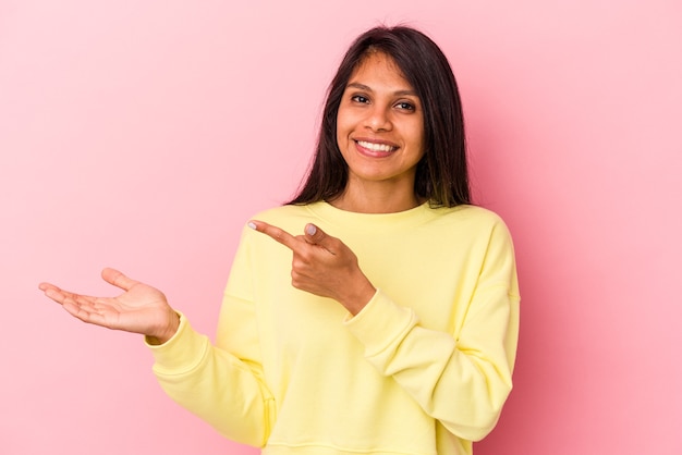 Jeune femme latine isolée sur fond rose excitée tenant un espace de copie sur la paume.