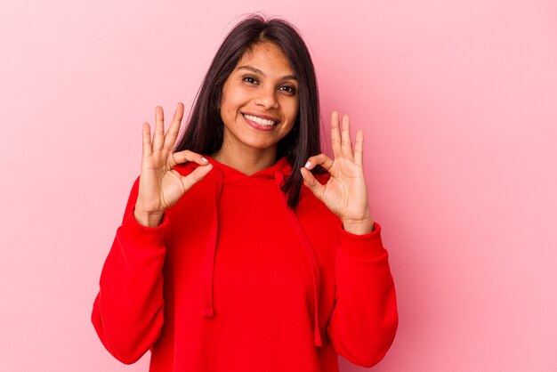 Jeune femme latine isolée sur fond rose joyeuse et confiante montrant un geste correct.