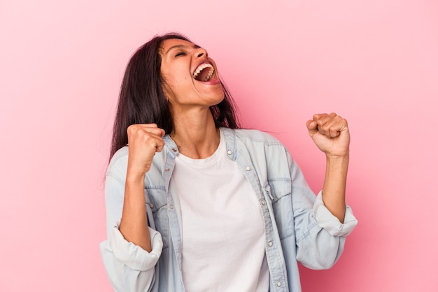 Jeune femme latine isolée sur fond rose levant le poing après une victoire, concept gagnant.