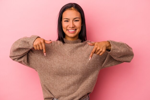 Jeune femme latine isolée sur fond rose pointe vers le bas avec les doigts, sentiment positif.