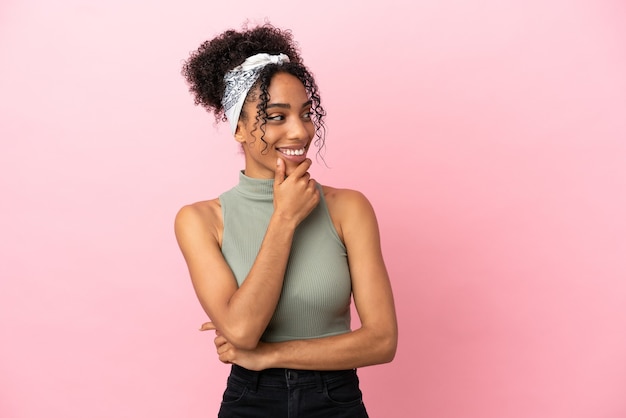 Jeune femme latine isolée sur fond rose regardant sur le côté et souriant