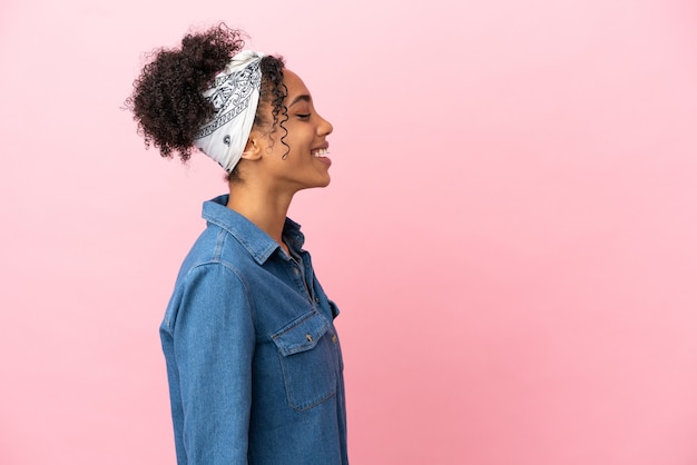 Jeune femme latine isolée sur fond rose en riant en position latérale