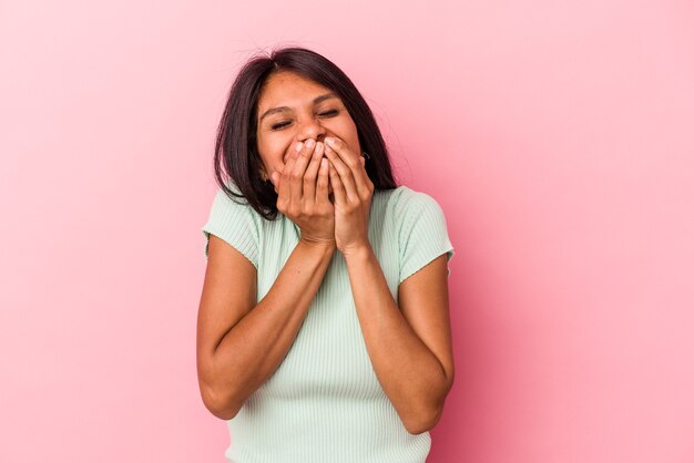 Jeune femme latine isolée sur fond rose en riant de quelque chose, couvrant la bouche avec les mains.