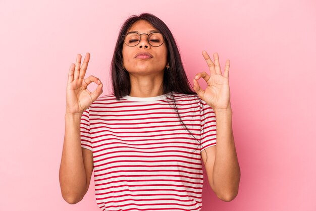 Jeune femme latine isolée sur fond rose se détend après une dure journée de travail, elle fait du yoga.