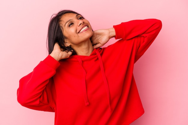 Jeune femme latine isolée sur fond rose se sentant confiante, les mains derrière la tête.