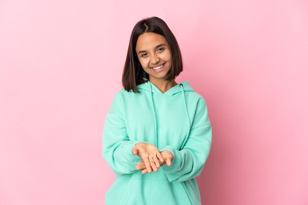 Jeune femme latine isolée sur fond rose tenant copyspace imaginaire sur la paume pour insérer une annonce