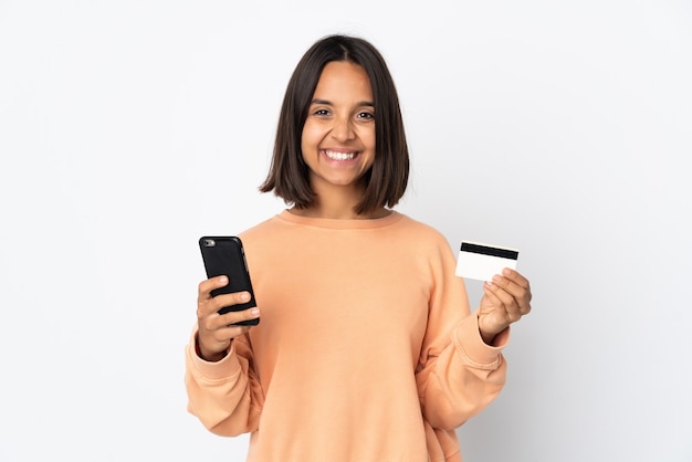 Jeune femme latine isolée sur un mur blanc acheter avec le mobile avec une carte de crédit