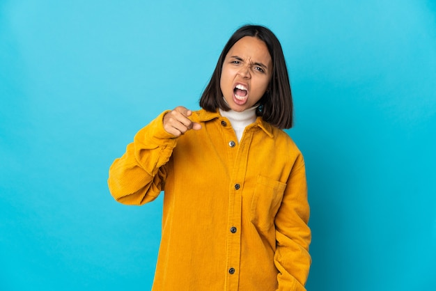 Jeune femme latine isolée sur un mur bleu frustré et pointant vers l'avant