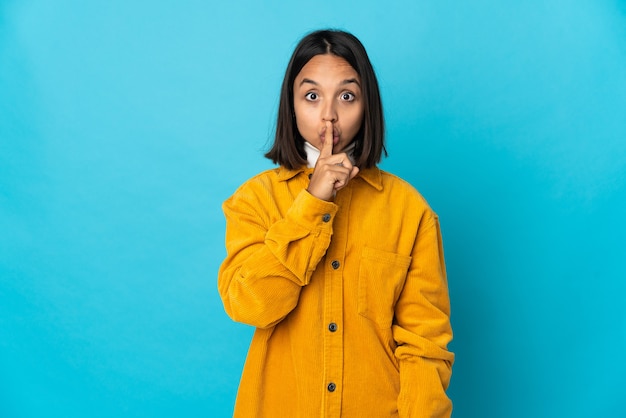 Jeune femme latine isolée sur un mur bleu montrant un signe de silence geste mettant le doigt dans la bouche