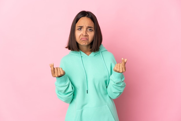 Jeune femme latine isolée sur un mur rose faisant un geste d'argent mais est ruinée