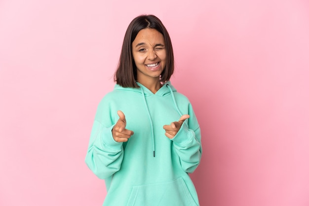 Jeune femme latine isolée sur un mur rose pointant vers l'avant et souriant