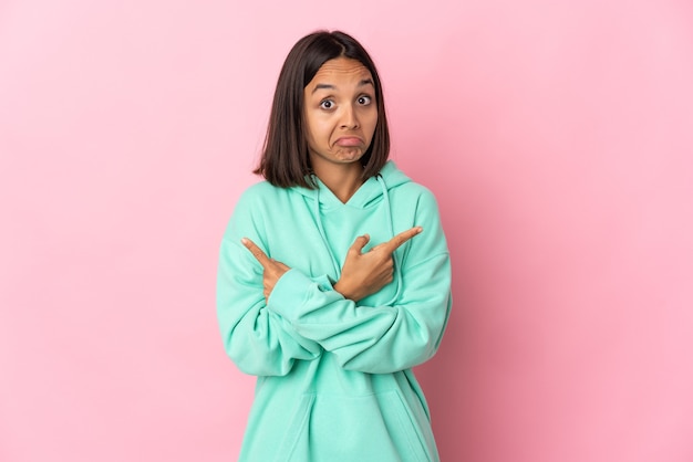 Jeune femme latine isolée sur une surface rose pointant vers les latéraux ayant des doutes