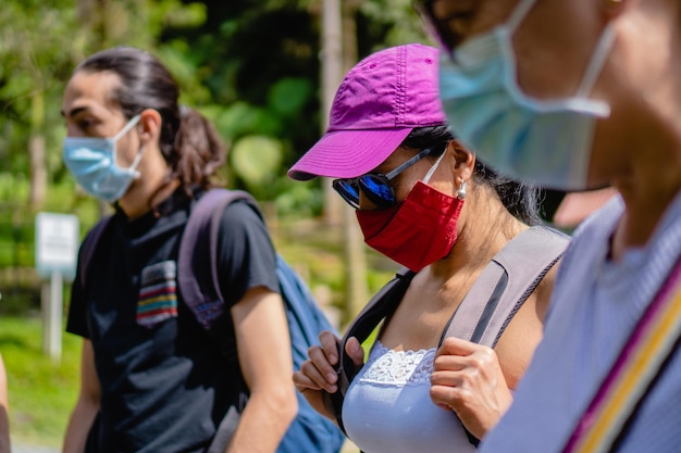 Jeune femme latine avec un masque en tissu rouge entouré de personnes avec des masques médicaux jetables dans un climat tropical de parc naturel