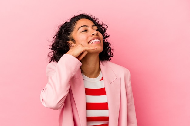 Jeune femme latine à la mode isolée sur fond rose montrant un geste d'appel de téléphone portable avec les doigts.