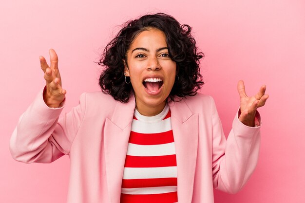 Photo jeune femme latine à la mode isolée sur fond rose recevant une agréable surprise, excitée et levant les mains.