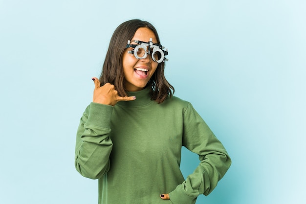 Jeune femme latine oculiste sur mur isolé montrant un geste d'appel de téléphone mobile avec les doigts.