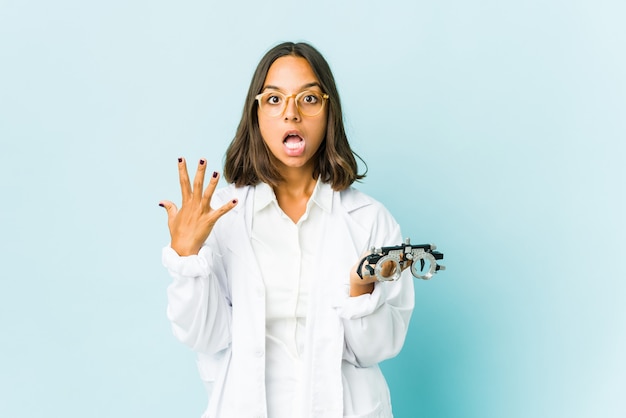 Jeune femme latine oculiste sur mur isolé montrant le numéro dix avec les mains.