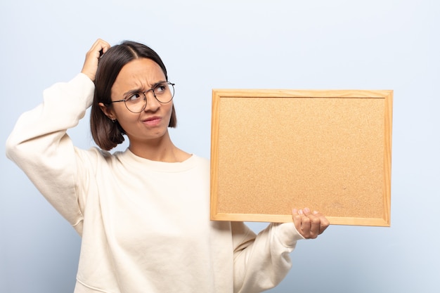 Jeune femme latine perplexe et confuse, se gratte la tête et regarde sur le côté