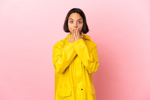 Jeune femme latine portant un manteau imperméable sur fond isolé couvrant la bouche avec la main