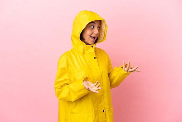 Jeune femme latine portant un manteau imperméable sur fond isolé avec une expression surprise tout en regardant de côté