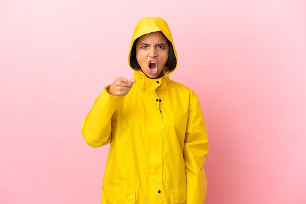 Jeune femme latine portant un manteau imperméable sur fond isolé frustré et pointant vers l'avant