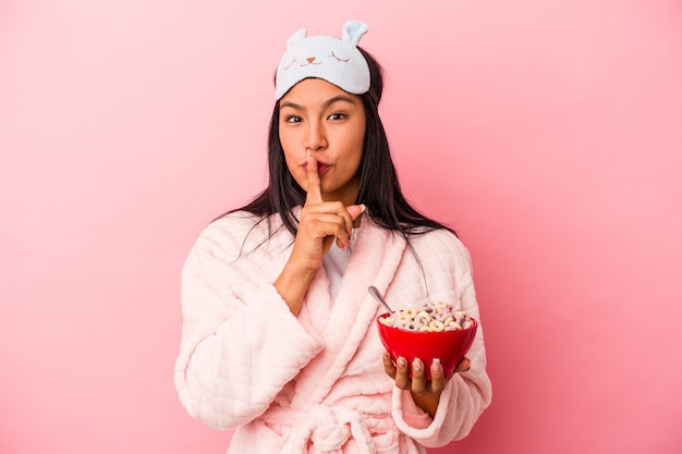 Jeune Femme Latine En Pyjama Tenant Un Bol De Céréales Isolé Sur Fond Rose Gardant Un Secret Ou Demandant Le Silence.