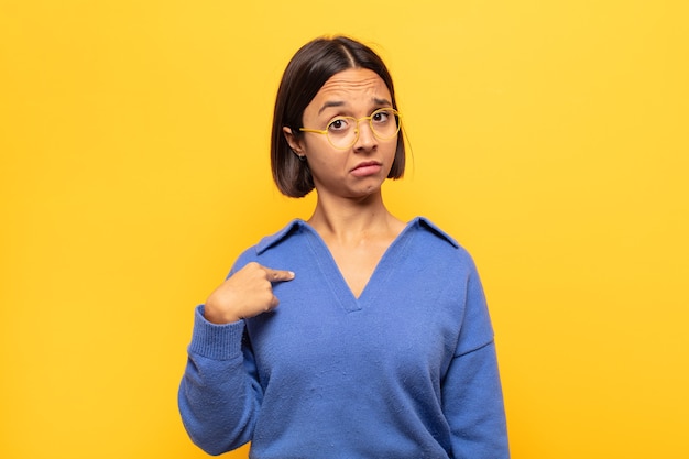 Jeune femme latine à la recherche de plaisir, fier et surpris, pointant joyeusement vers soi, se sentant confiant et élevé