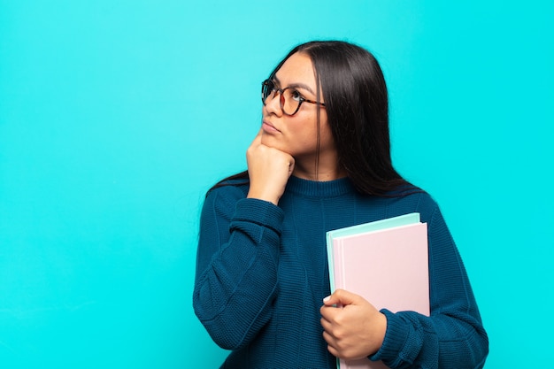 Jeune femme latine avec un regard concentré, se demandant avec une expression douteuse, regardant vers le haut et sur le côté