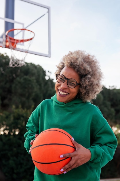 Jeune femme latine riant sur un terrain de basket avec un ballon dans ses mains concept de sport urbain dans l'espace de copie de rue pour le texte