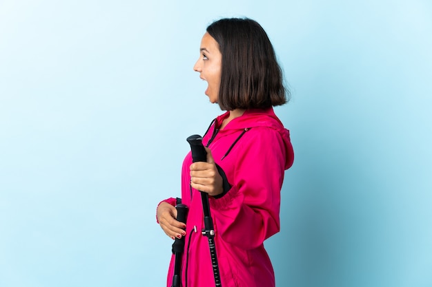 Jeune femme latine avec sac à dos et bâtons de randonnée bleu riant en position latérale