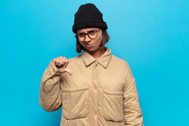 Photo jeune femme latine se sentant cross, en colère, ennuyé, déçu ou mécontent, montrant les pouces vers le bas avec un regard sérieux