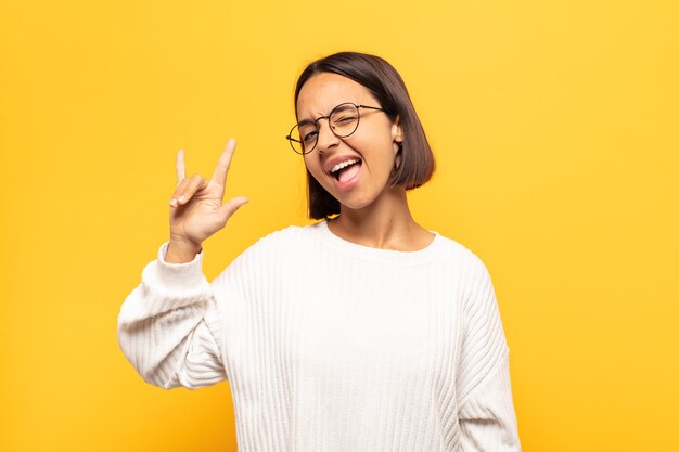 Jeune femme latine se sentant heureuse, amusante, confiante, positive et rebelle, faisant du rock ou du heavy metal signe avec la main