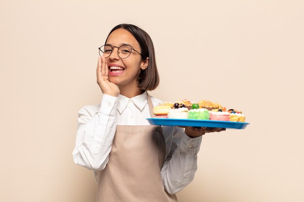 Jeune femme latine se sentant heureuse, excitée et positive, donnant un grand cri avec les mains à côté de la bouche, appelant