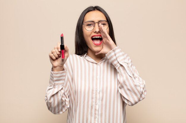 Jeune femme latine se sentant heureuse, excitée et positive, donnant un grand cri avec les mains à côté de la bouche, appelant