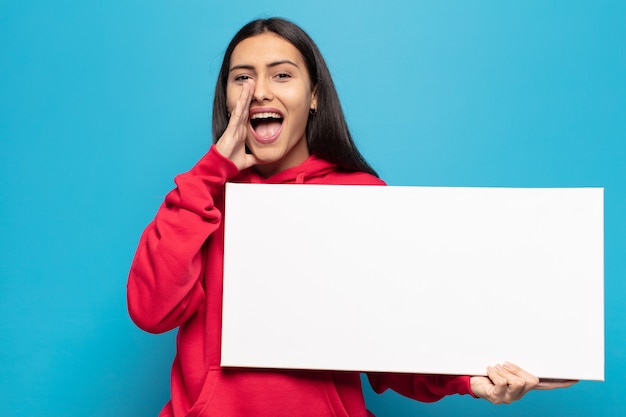 Jeune femme latine se sentant heureuse, excitée et positive, donnant un grand cri avec les mains à côté de la bouche, appelant