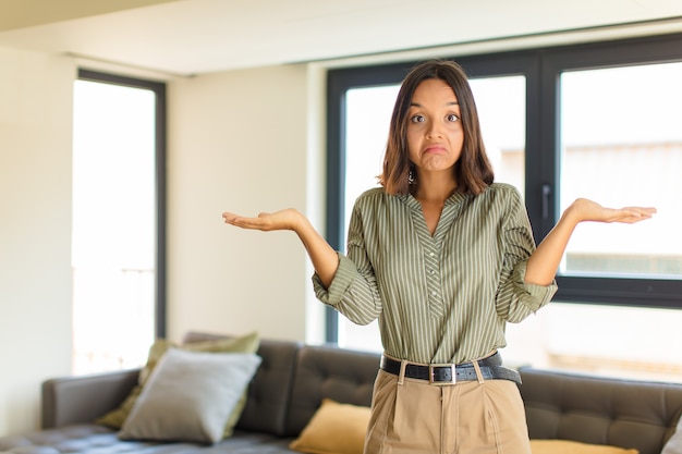 Jeune femme latine se sentant perplexe et confus, doutant, pondérant ou choisissant différentes options avec une expression drôle