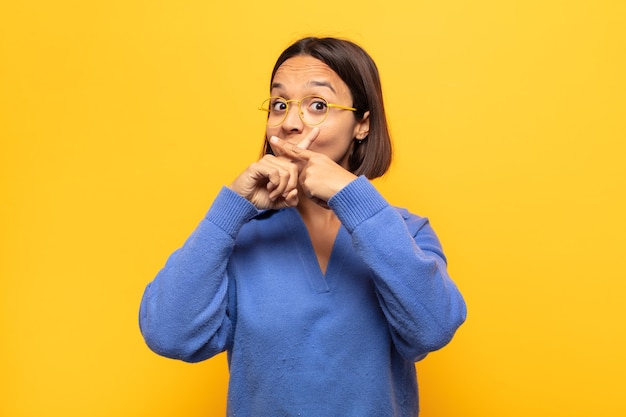 Jeune femme latine à la sérieuse et mécontente avec les deux doigts croisés à l'avant dans le rejet, demandant le silence