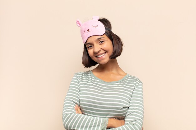 Jeune femme latine souriant à la caméra avec les bras croisés et une expression heureuse, confiante, satisfaite, vue latérale