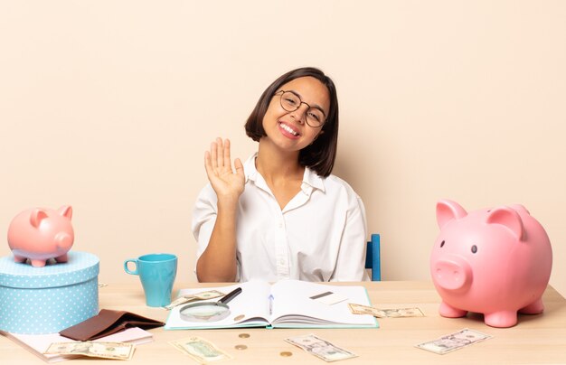 Jeune femme latine souriant joyeusement et joyeusement, en agitant la main, en vous accueillant et en vous saluant, ou en disant au revoir