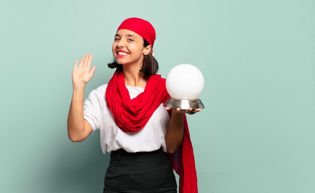 Jeune femme latine souriant joyeusement et joyeusement, en agitant la main, en vous accueillant et en vous saluant, ou en vous disant au revoir