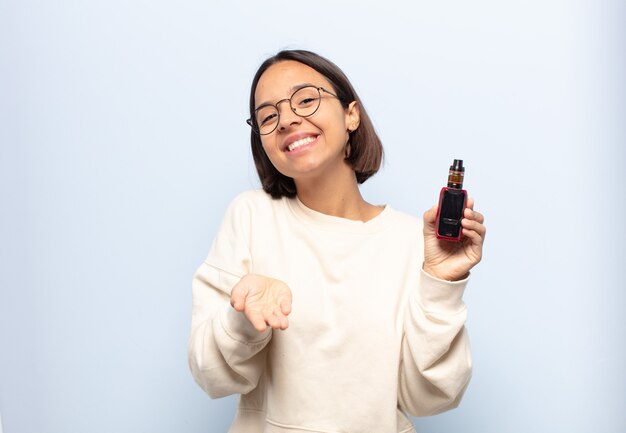 Jeune femme latine souriant joyeusement avec un regard amical, confiant et positif, offrant et montrant un objet ou un concept